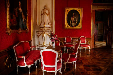 Valtice, Southern Moravia, Czech Republic, 04 July 2021: Castle interior with baroque wooden carved furniture, dining room or red salon with ceramic tiled stove, porcelain vase on table, soft chairs.のeditorial素材