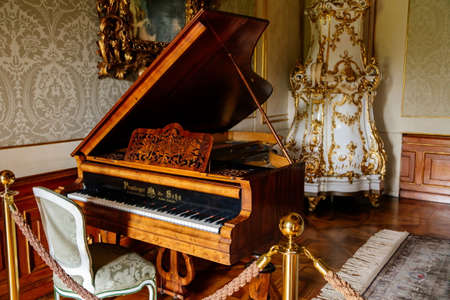Valtice, Southern Moravia, Czech Republic, 04 July 2021: Castle interior, baroque wooden carved furniture, music room with antique grand piano, white ceramic tiled stove, tall mirror in gilded frame.のeditorial素材