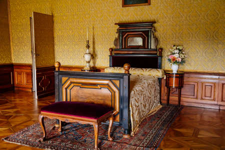 Valtice, Southern Moravia, Czech Republic, 04 July 2021: Castle interior with baroque wooden carved furniture, yellow bedroom with bed near secret door, beautiful romantic chateau, flowers in vase.のeditorial素材