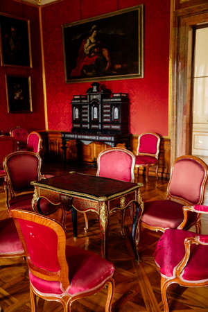 Valtice, Southern Moravia, Czech Republic, 04 July 2021: Castle interior with baroque wooden carved furniture, red salon, inlaid table with gilding, bureau with swing doors, wooden secretaire.のeditorial素材