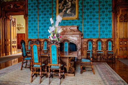 Lednice, Southern Moravia, Czech Republic, 04 July 2021: Castle interior with neo-gothic wooden carved ceiling and furniture, blue salon, table with chairs, open marble fireplace, vase with flowers.のeditorial素材