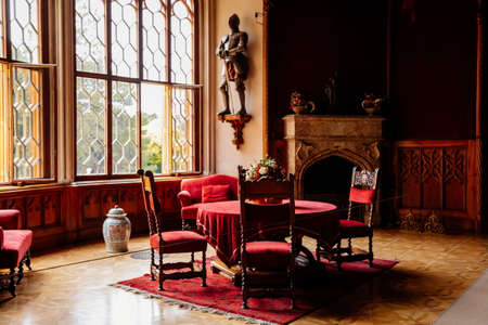 Lednice, Southern Moravia, Czech Republic, 04 July 2021: Castle interior with neo-gothic wooden carved ceiling and furniture, red salon, table with chairs and sofa, open marble fireplace, chandelier.のeditorial素材