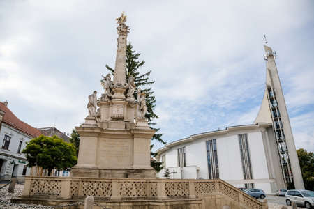 Hustopece, Southern Moravia, Czech Republic, 04 July 2021: Modern Church of St. Wenceslas and St. Agnes Czech with spire and baroque Holy Trinity Column with stone statues of saints at main square.のeditorial素材