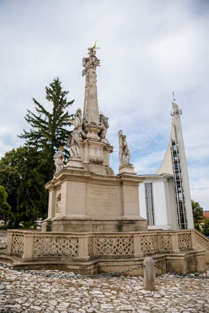 Hustopece, Southern Moravia, Czech Republic, 04 July 2021: Modern Church of St. Wenceslas and St. Agnes Czech with spire and baroque Holy Trinity Column with stone statues of saints at main square.のeditorial素材