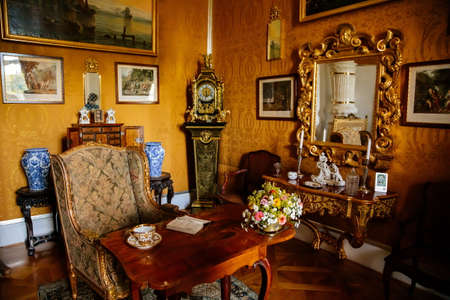 Vranov nad dyji, Southern Moravia, Czech Republic, 03 July 2021: Castle interior with baroque wooden carved furniture, writing desk, mirror in gilded frame, porcelain figurines, grandfather clock.のeditorial素材
