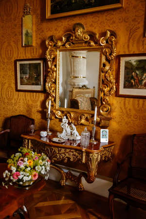 Vranov nad dyji, Southern Moravia, Czech Republic, 03 July 2021: Castle interior with baroque wooden carved furniture, writing desk, mirror in gilded frame, porcelain figurines, grandfather clock.のeditorial素材