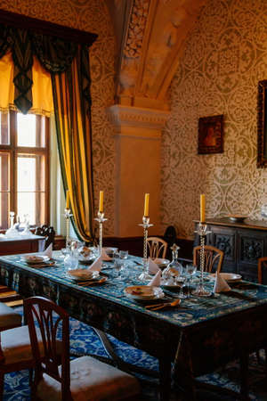 Cervena Lhota, South Bohemia, Czech Republic, 9 October 2021: Castle interior, baroque wooden carved furniture, dining room with floral ornaments on walls, porcelain set on table, glass candlesticksのeditorial素材