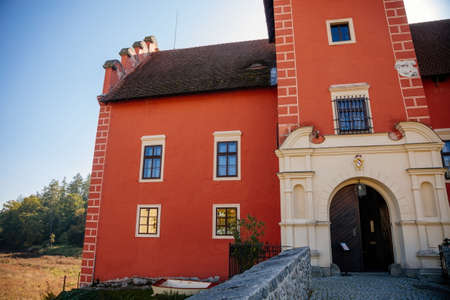 Cervena Lhota, South Bohemia, Czech Republic, 9 October 2021: Beautiful small romantic red water chateau, Antique castle with fall color at sunny autumn day, stone bridge and entrance gateのeditorial素材