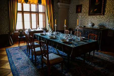 Cervena Lhota, South Bohemia, Czech Republic, 9 October 2021: Castle interior, baroque wooden carved furniture, dining room with floral ornaments on walls, porcelain set on table, glass candlesticksのeditorial素材
