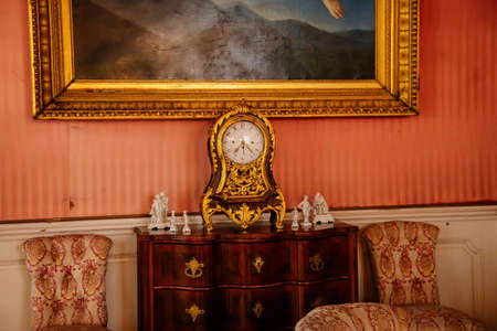 Libochovice, Bohemia, Czech Republic, 19 September 2021: Castle interior with baroque wooden furniture, gold plated antique clock on dresser with drawers, picture in gilded frame on wallのeditorial素材