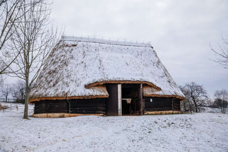 Kourim, Czech Republic, 26 December 2021: Traditional village wooden timbered barn with low walls and steep thatched roof in winter, historic country-style architecture, open-air ethnographic museumのeditorial素材