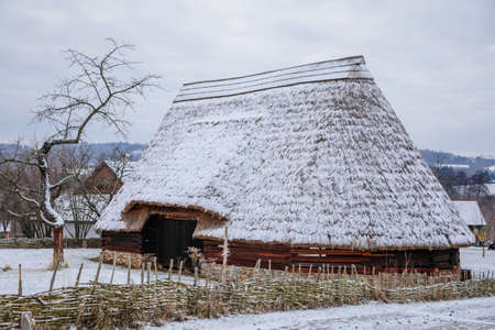Kourim, Czech Republic, 26 December 2021: Traditional village wooden timbered barn with low walls and steep thatched roof in winter, historic country-style architecture, open-air ethnographic museumのeditorial素材