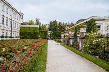 Salzburg, Austria, 28 August 2021: Famous Mirabell gardens near palace, geometrically arranged park, green grass and flowers at summer day, was featured in Sound of Music, Red roses and stone vases