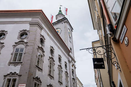 Salzburg, Austria, 28 August 2021: Grain Lane or Getreidegasse famous shopping narrow street in historic Altstadt, wrought iron guild signs at summer day, Rathaus Old Town Hall with clock towerのeditorial素材