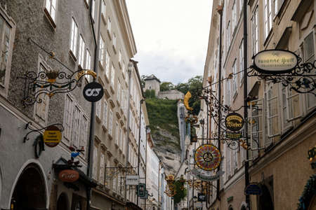 Salzburg, Austria, 28 August 2021: Grain Lane or Getreidegasse famous shopping narrow street in historic Altstadt or Old Town, wrought iron guild signs at summer day, numerous high townhouses skylineのeditorial素材