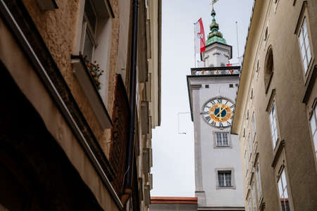 Salzburg, Austria, 28 August 2021: Grain Lane or Getreidegasse famous shopping narrow street in historic Altstadt, wrought iron guild signs at summer day, Rathaus Old Town Hall with clock towerのeditorial素材