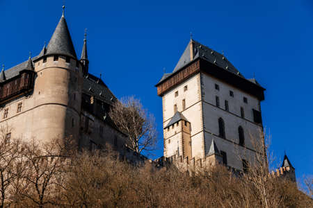 Karlstejn, Bohemia, Czech Republic, 12 March 2022: old royal medieval gothic castle with tower founded by king Charles IV, blue sky at sunny spring day, famous landmark, battlements fortified wallsのeditorial素材