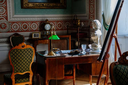 Litomysl, Czech Republic, 17 April 2022: castle chateau interior with baroque classic furniture, wooden writing desk and chair near windows, Photos, figurines and documents, lamp with green shadeのeditorial素材