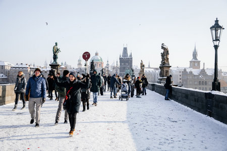 Prague, Czech Republic, 15 December 2022: Old town bridge towers with spire, River Vltava, View from Charles bridge, snow on sunny winter day, baroque sculptures and lampposts, tourists follow guideのeditorial素材