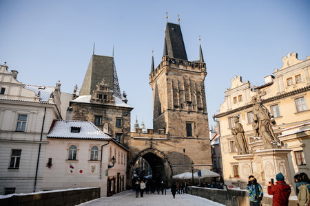 Prague, Czech Republic, 15 December 2022: Lesser Town with Mala Strana bridge towers with spire above River Vltava, View from Charles bridge, snow on sunny winter day, baroque sculptures and lamppostsのeditorial素材