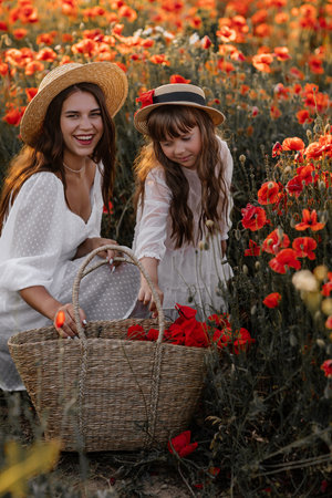 Beautiful young woman with girl in field with poppies, mother and daughter in white dresses and straw hats in evening at sunset, Summer countryside nature flowers, family relaxing, Rural simple lifeの写真素材
