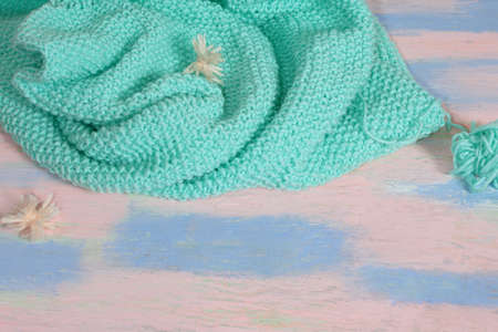 Knitted turquoise sweater with a ball of wool yarn and on a pink-blue tableの写真素材
