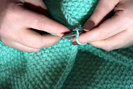 Womans hands , which gently knit a turquoise sweater with steel knitting needles.の写真素材