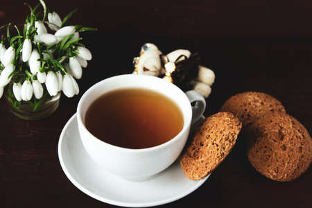 snowdrops in a vase, a cup of tea and biscotti on the tableの写真素材