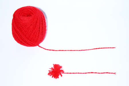 A red ball of wool yarn for knitting and a pompon made of yarn on a white backgroundの写真素材