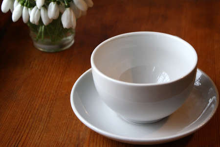 White cup for tea on a white saucer on a wooden table and a bouquet of snowdrops in the cornerの写真素材