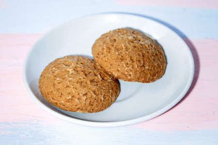 Two round fresh oatmeal cookies on a white saucer on a pink and blue boardの写真素材