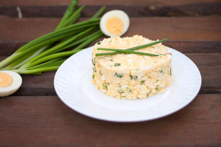 Egg salad with green onions on a white plate against wooden backgroundの写真素材