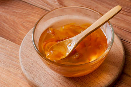 Piala with a spoon in homemade peach jam on a wooden round stand on the table in the morning sun....