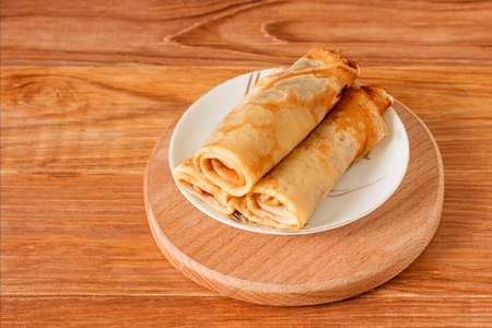 Several delicious homemade pancakes are rolled up on a saucer on a wooden background. Copy space