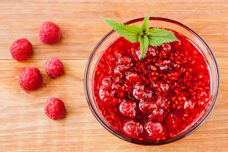 Glass small saucer with raspberry jam with fresh raspberries and mint close-up on wooden background. Top viewの写真素材
