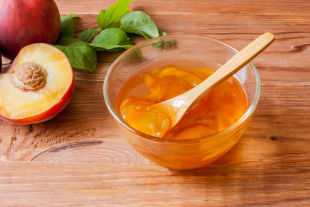 Piala with a spoon in homemade peach jam on a wooden round stand on the table in the morning sun. The concept of homemade conservation.の写真素材