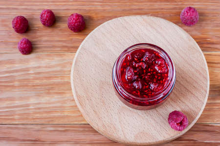 Glass small saucer with raspberry jam with fresh raspberries close up on wooden background. Top viewの写真素材