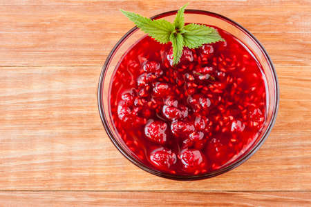 Glass small saucer with raspberry jam with fresh raspberries and mint close-up on wooden background. Top viewの写真素材
