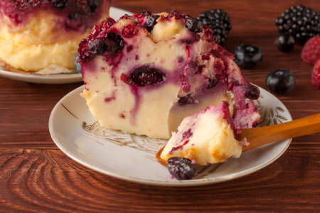 Delicious cottage cheese casserole with berries, cottage cheese pudding with berries. Appetizing fresh cottage cheese casserole with blueberries, raspberries and blackberries on a wooden table.の写真素材