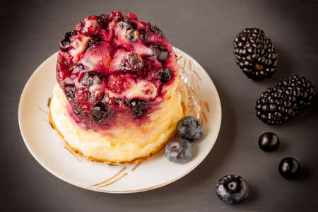 Delicious cottage cheese casserole with berries, cottage cheese pudding with berries. Appetizing fresh cottage cheese casserole with blueberries, raspberries and blackberries on a dark background.の写真素材