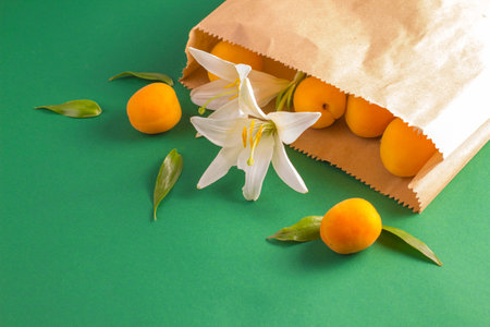 Ripe apricots and lily flowers in a kraft paper bag on a green background. Waste-free shopping concept, reusable eco-friendly packagingの写真素材