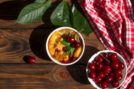 A portioned plate with clafoutis on a wooden background on a bright sunny day. Traditional French pie with cherry clafoutis. Top viewの写真素材