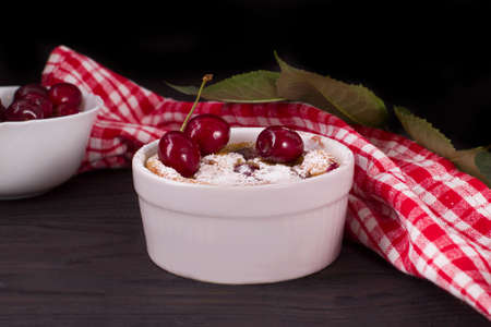 Portion plate with clafoutis sprinkled with powdered sugar on a wooden background. Traditional French pie with cherry clafoutisの写真素材
