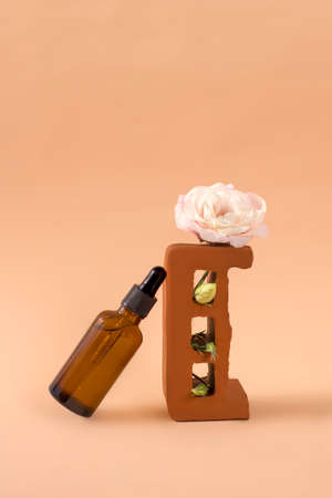 Amber glass bottle for cosmetics, natural skin care on a stone pedestal with an eustoma flower on a beige background. Alternative herbal medicine. Copy space.の写真素材