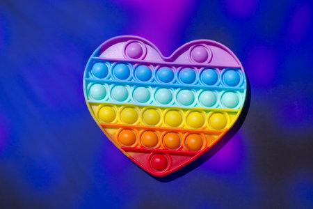Heart-shaped colorful silicone popping sensory toy on neon abstract background.の写真素材