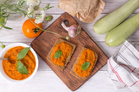 Dish with squash caviar decorated with basil on a white wooden background. Squash spread, zucchini caviar and ingredients. Healthy food. Top viewの写真素材