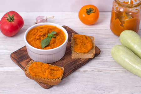 Dish with squash caviar decorated with basil on a white wooden background. Squash spread, zucchini caviar and ingredients. Healthy food. Top viewの写真素材