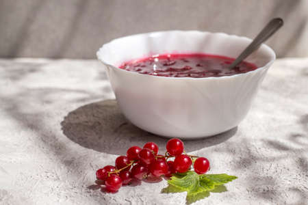 A dish with delicious freshly boiled red currant jam on a light table.