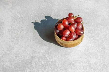 A bunch of red grapes on a light table with a hard shadow from sunlight with copy space.の写真素材