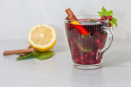 Red drink with fruits, lemon and cinnamon on a light background.